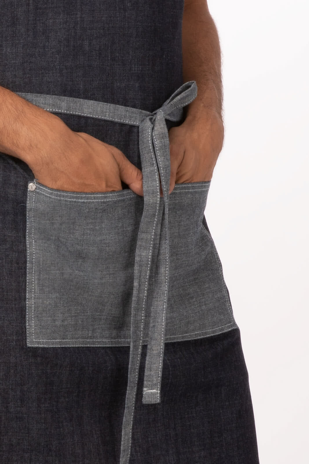 A dark indigo denim bib apron featuring a waist tie and a front pocket. It has branding on the fabric.