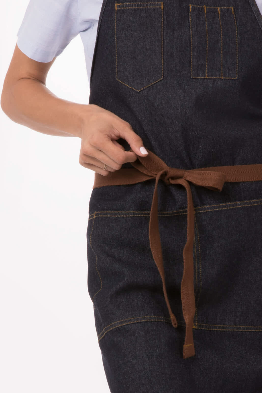 A denim apron in dark blue, featuring pockets and a brown tie belt, with a hand adjusting the waist strap.