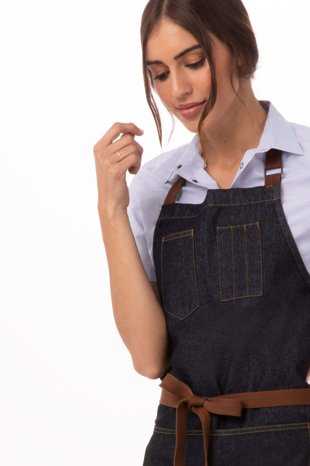 A denim apron in dark blue with brown leather straps, featuring multiple pockets and a branding logo.