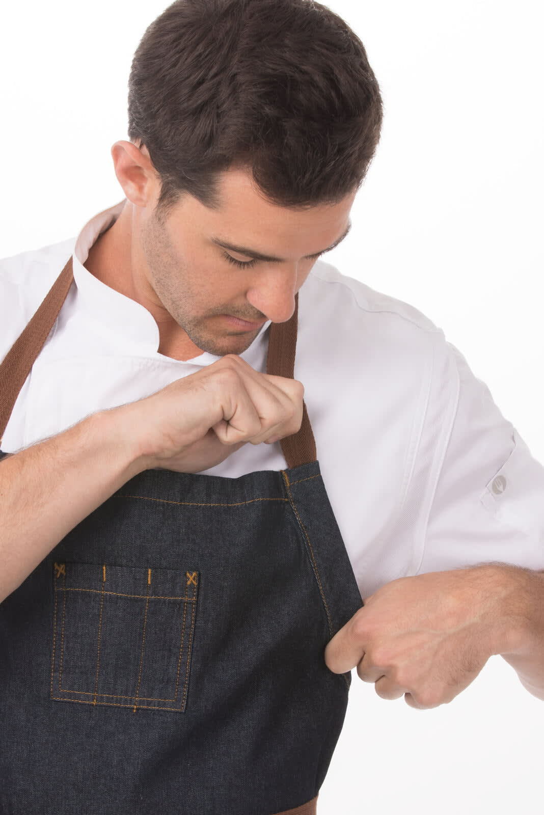 A stylish dark denim apron with brown straps worn by a chef adjusting it. The apron features a pocket and a logo.