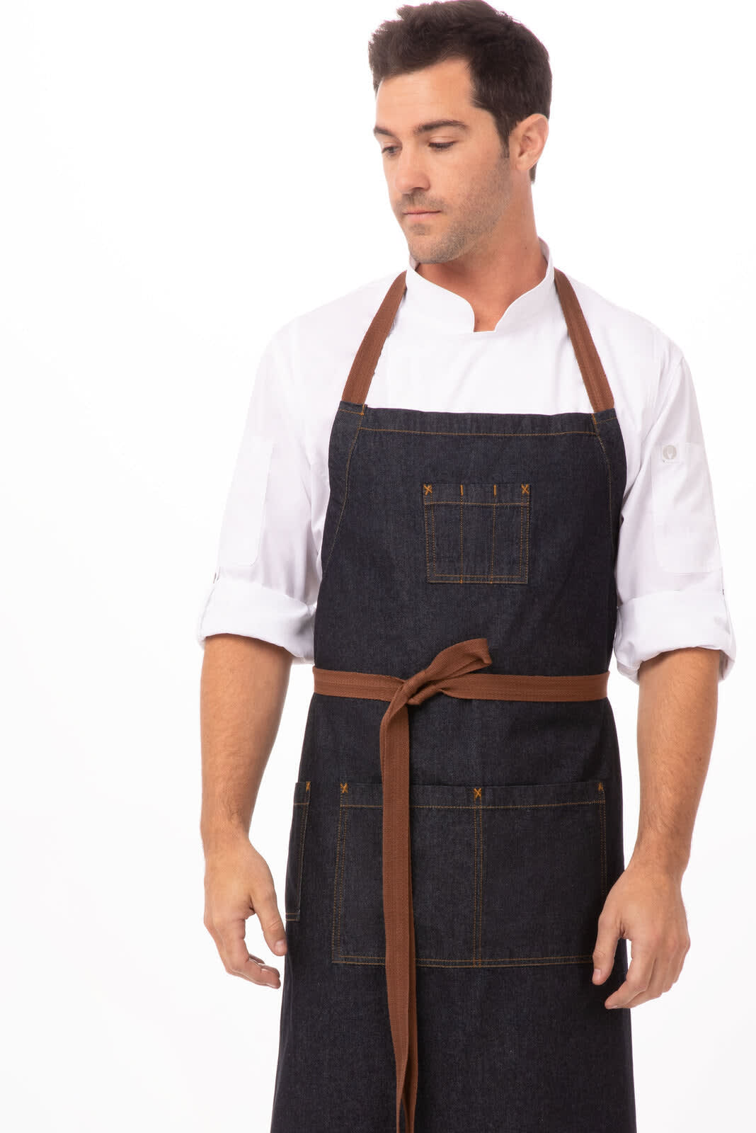 A denim bib apron in dark blue with brown straps, featuring front pockets and worn by a model.