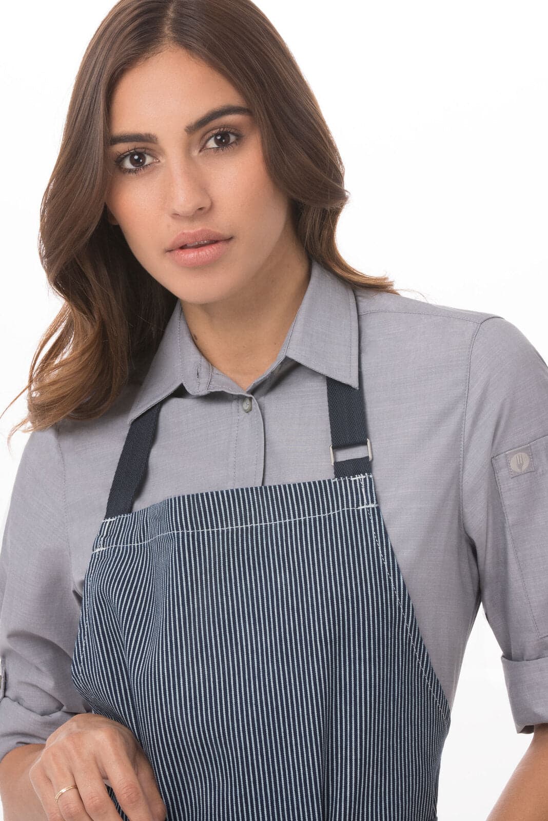 A woman is wearing a striped navy blue apron over a light grey shirt, featuring adjustable straps and a logo.