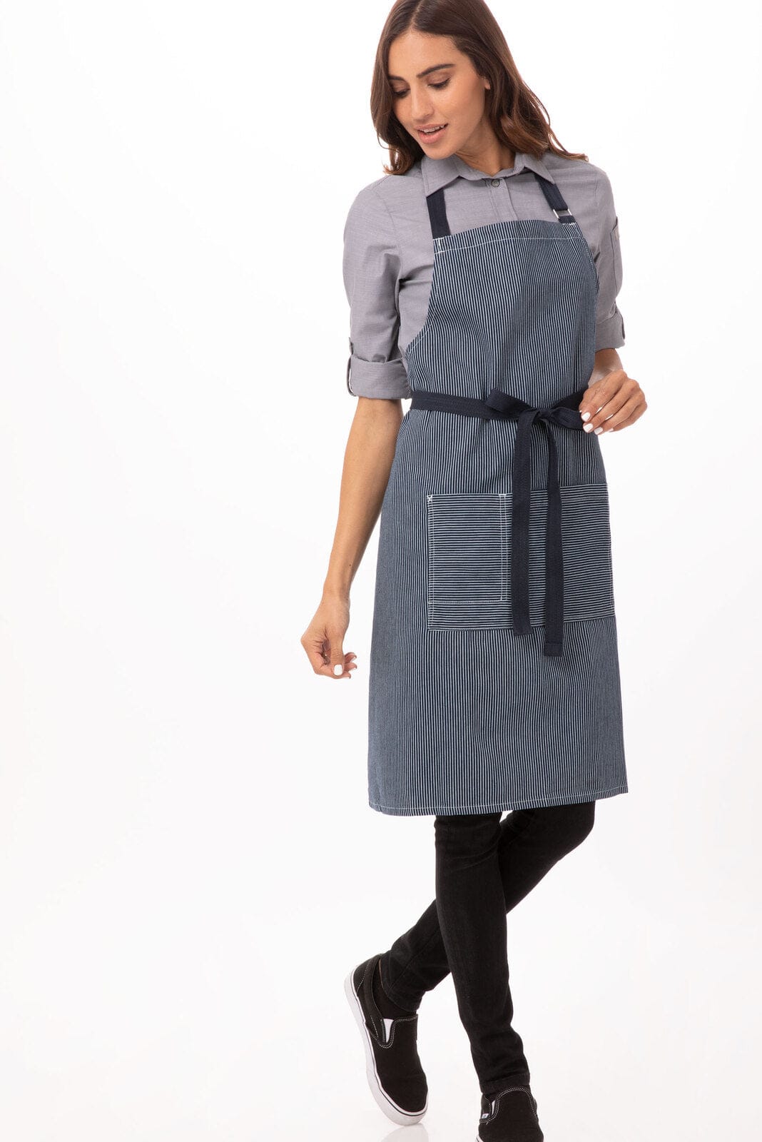 A woman wearing a navy blue Portland Bib Apron over a grey shirt, with pockets and a waist tie.