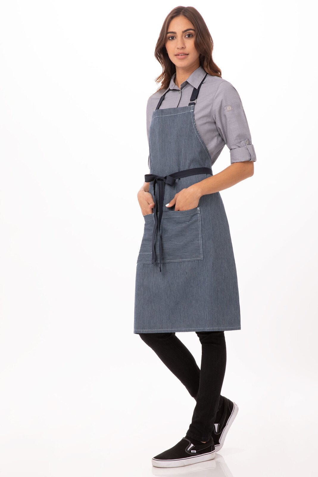A blue denim bib apron featuring a pocket and adjustable straps, worn by a model in a grey shirt.