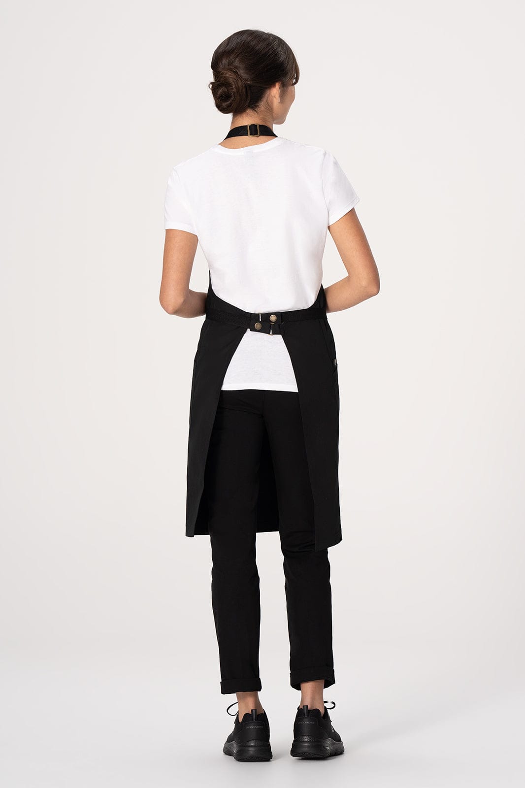 A black bib apron with a unique back design, worn over a white shirt and black pants, featuring a logo.