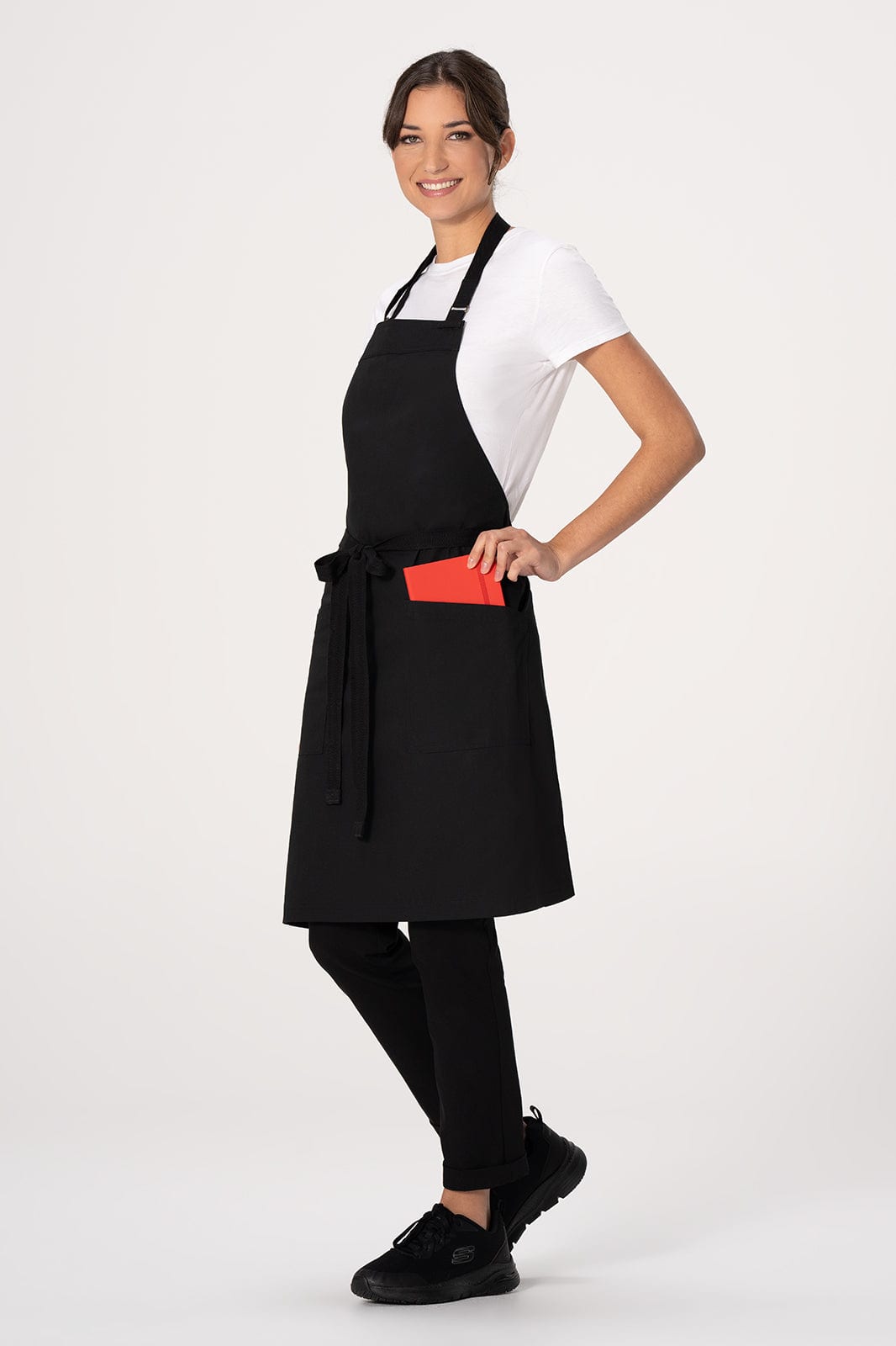 A black bib apron featuring a red pocket, worn by a model in a white t-shirt and black pants.