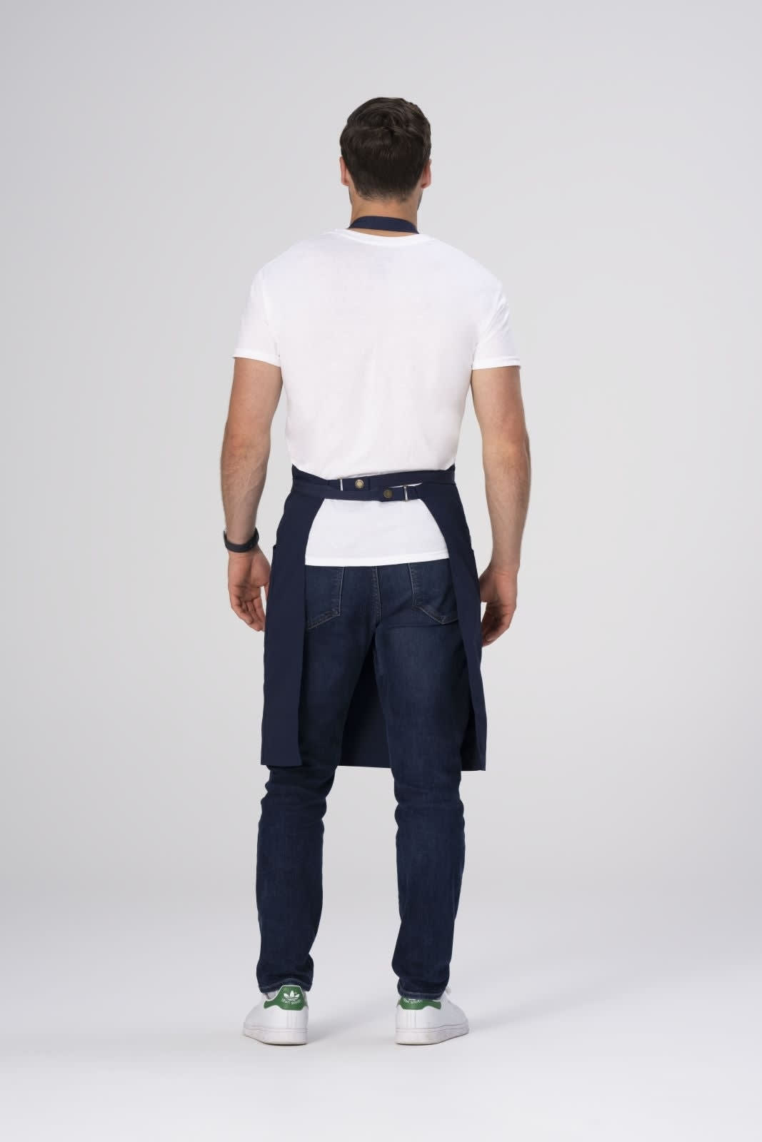 A person wears a navy Lockharte bib apron over a white t-shirt and jeans, with a logo visible on the apron.