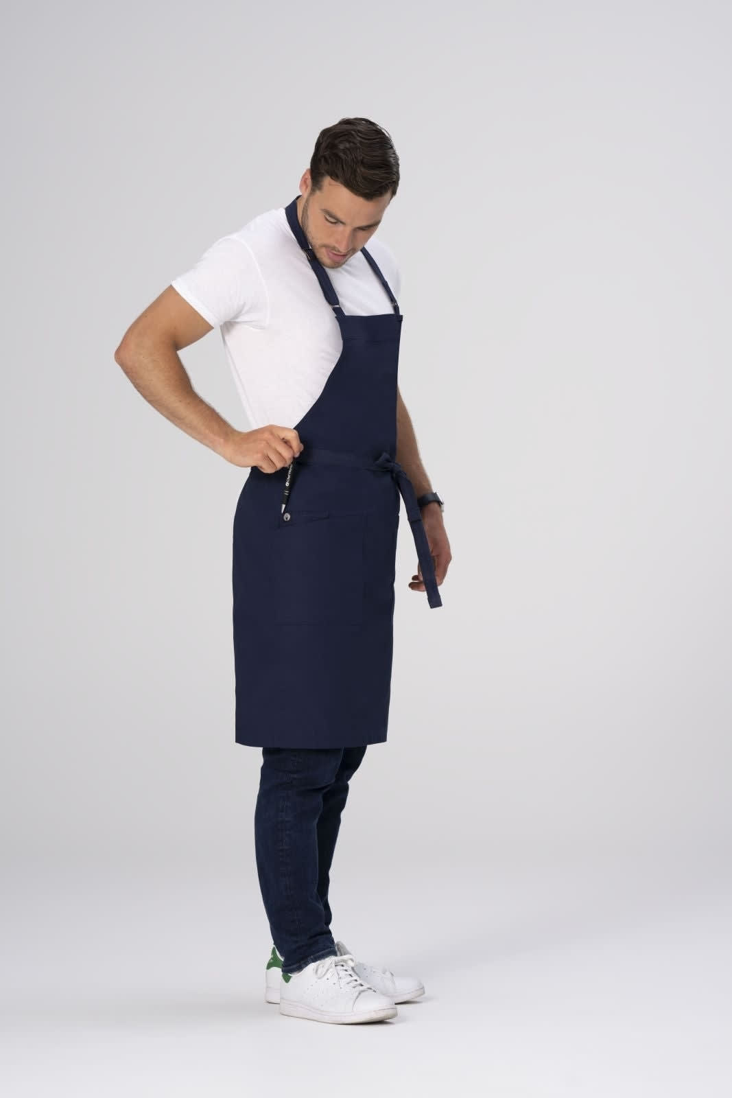 A man wearing a navy blue Lockharte bib apron over a white shirt and jeans, featuring a logo.