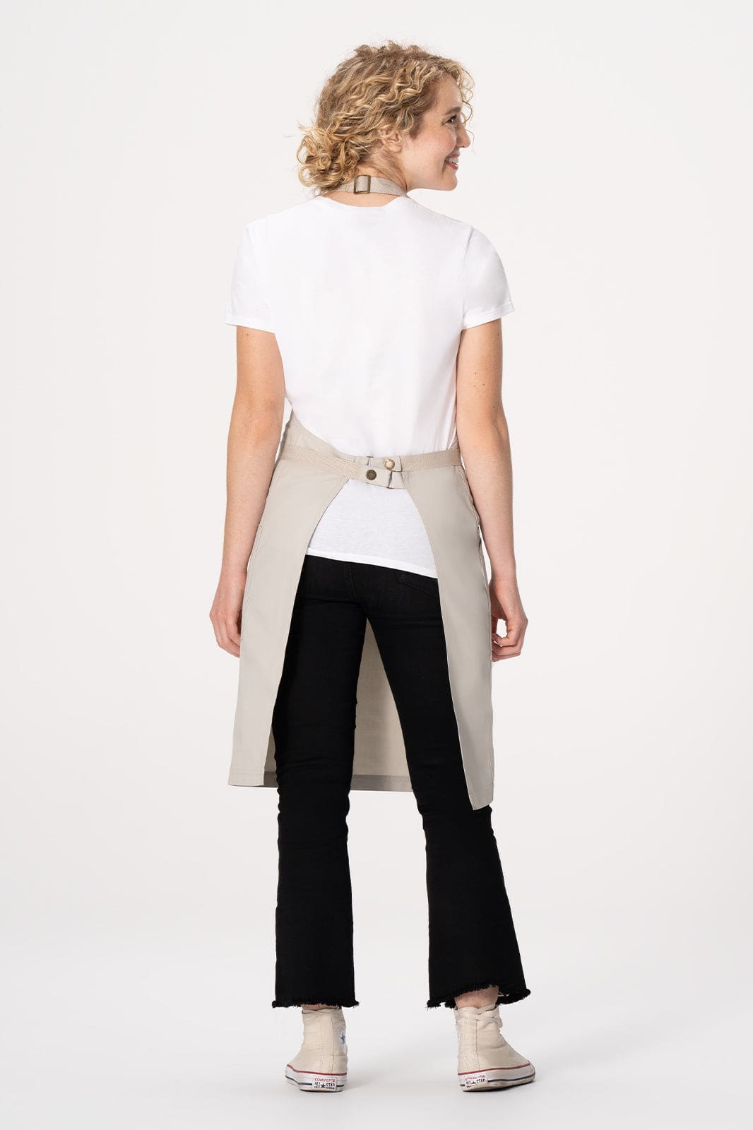 A beige Lockharte Bib Apron with a logo, worn over a white top, showing a back view of a model.