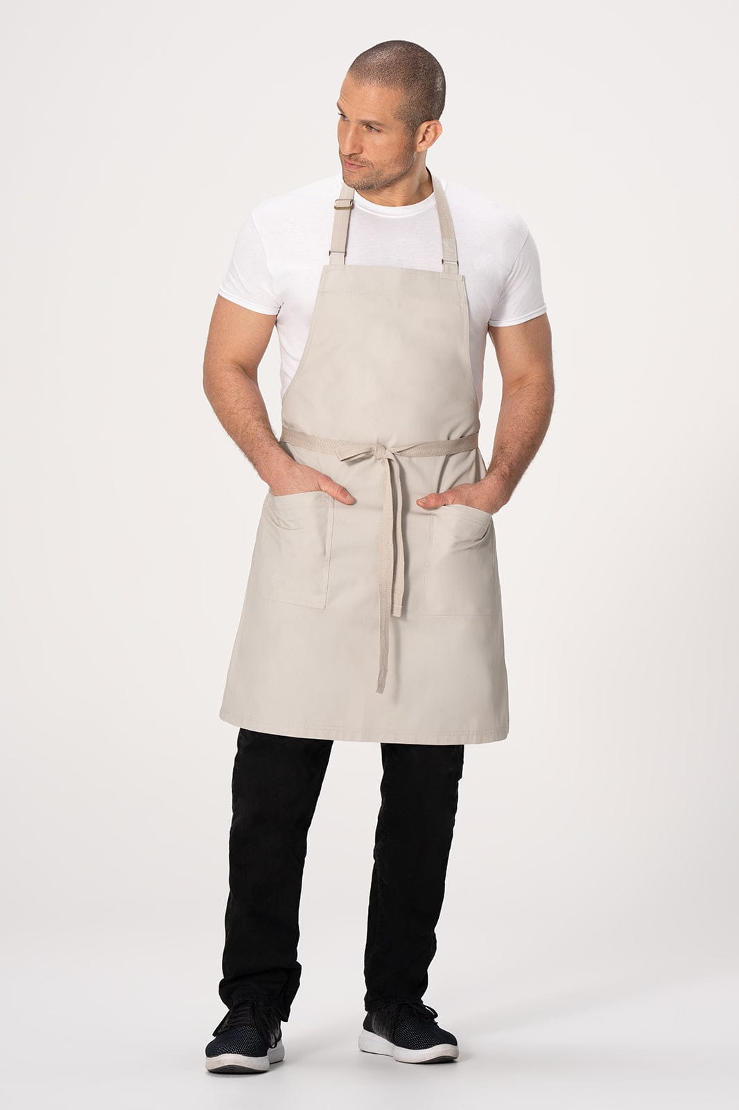 A beige bib apron worn by a model, featuring two front pockets and adjustable straps.