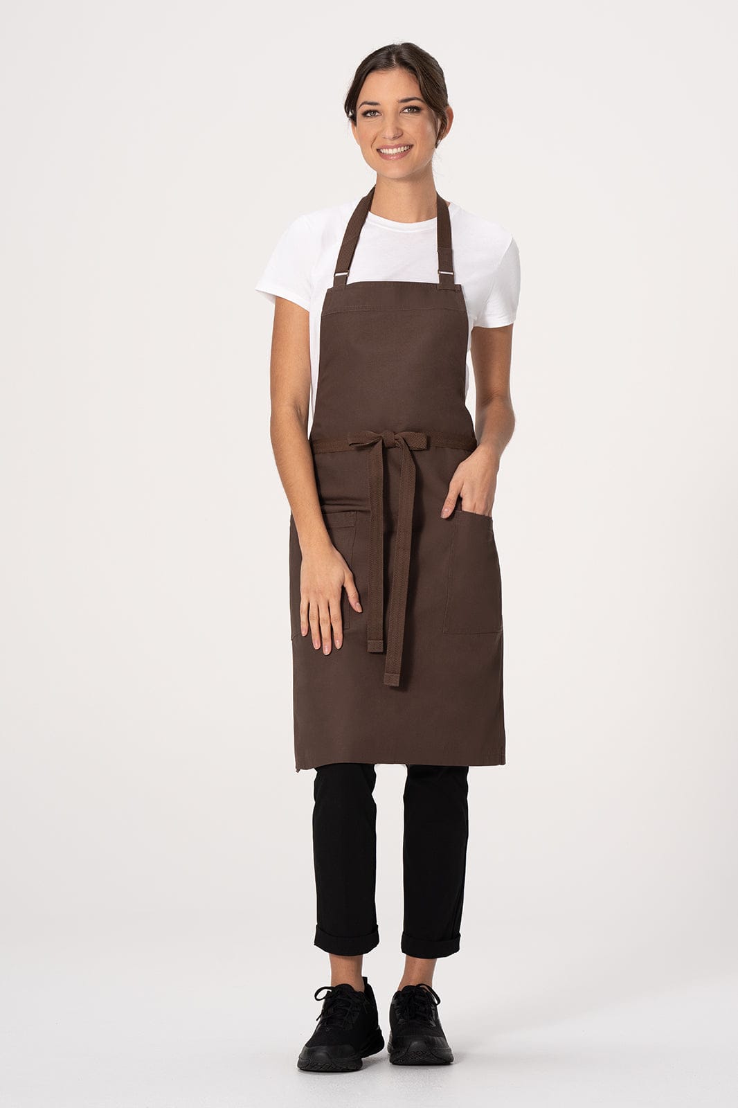 A brown bib apron with a waist tie, worn by a model in a white t-shirt and black pants, featuring a logo.