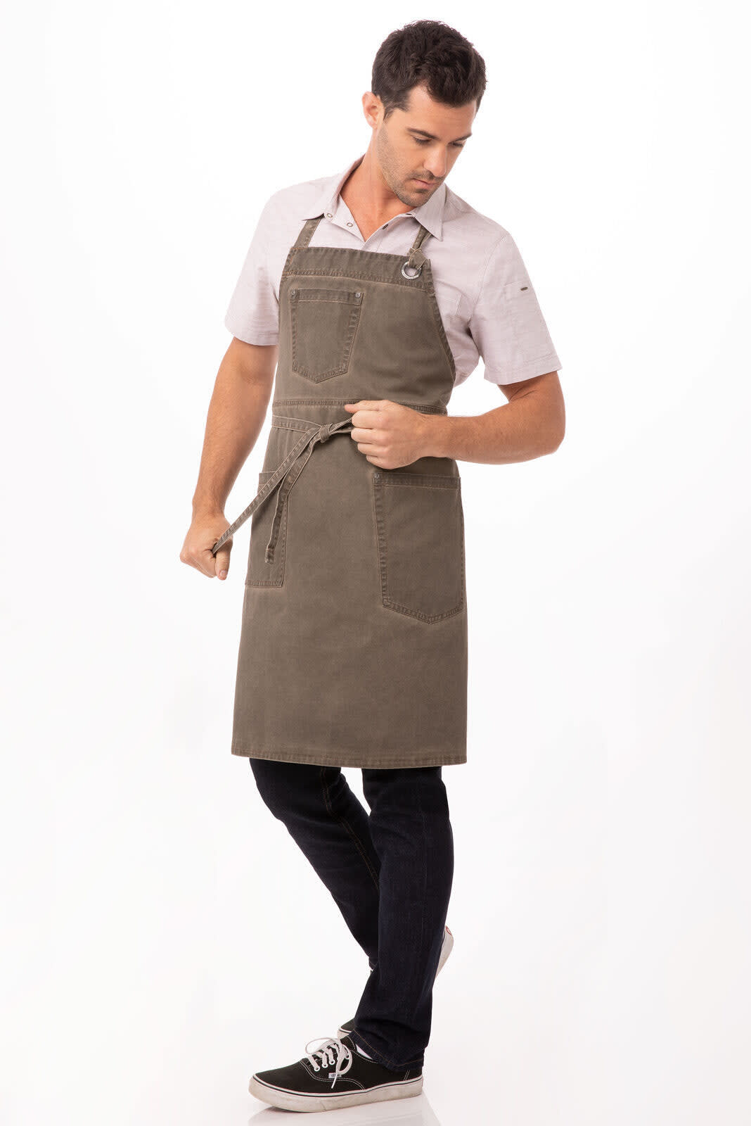 A man wearing a dark green Dorset Bib Apron with a front pocket, styled with a shirt and dark jeans.