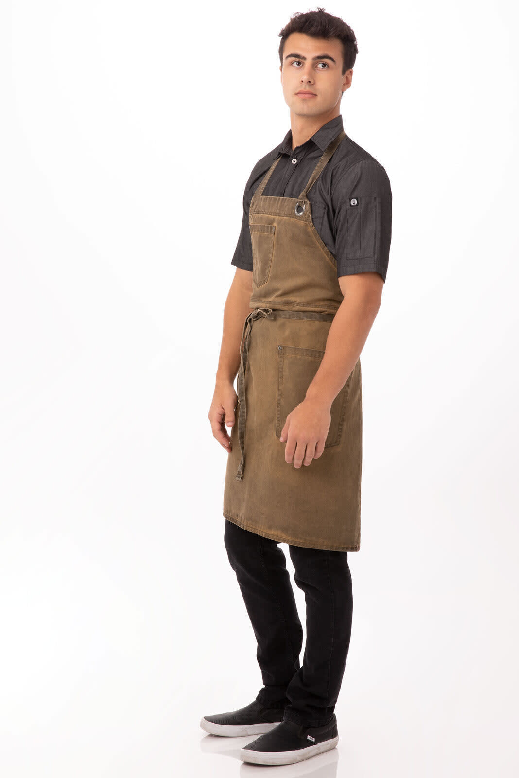 A man wearing a brown Dorset bib apron over a black shirt and black pants, with a logo visible on the apron.