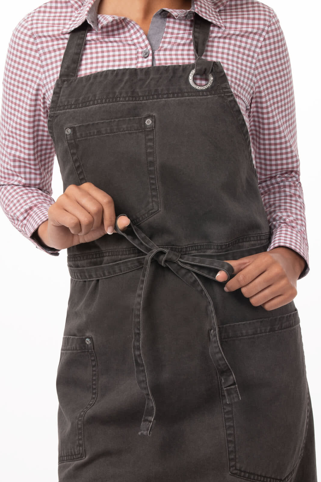 A dark grey bib apron with adjustable straps and pockets, worn by a person in a checked shirt.