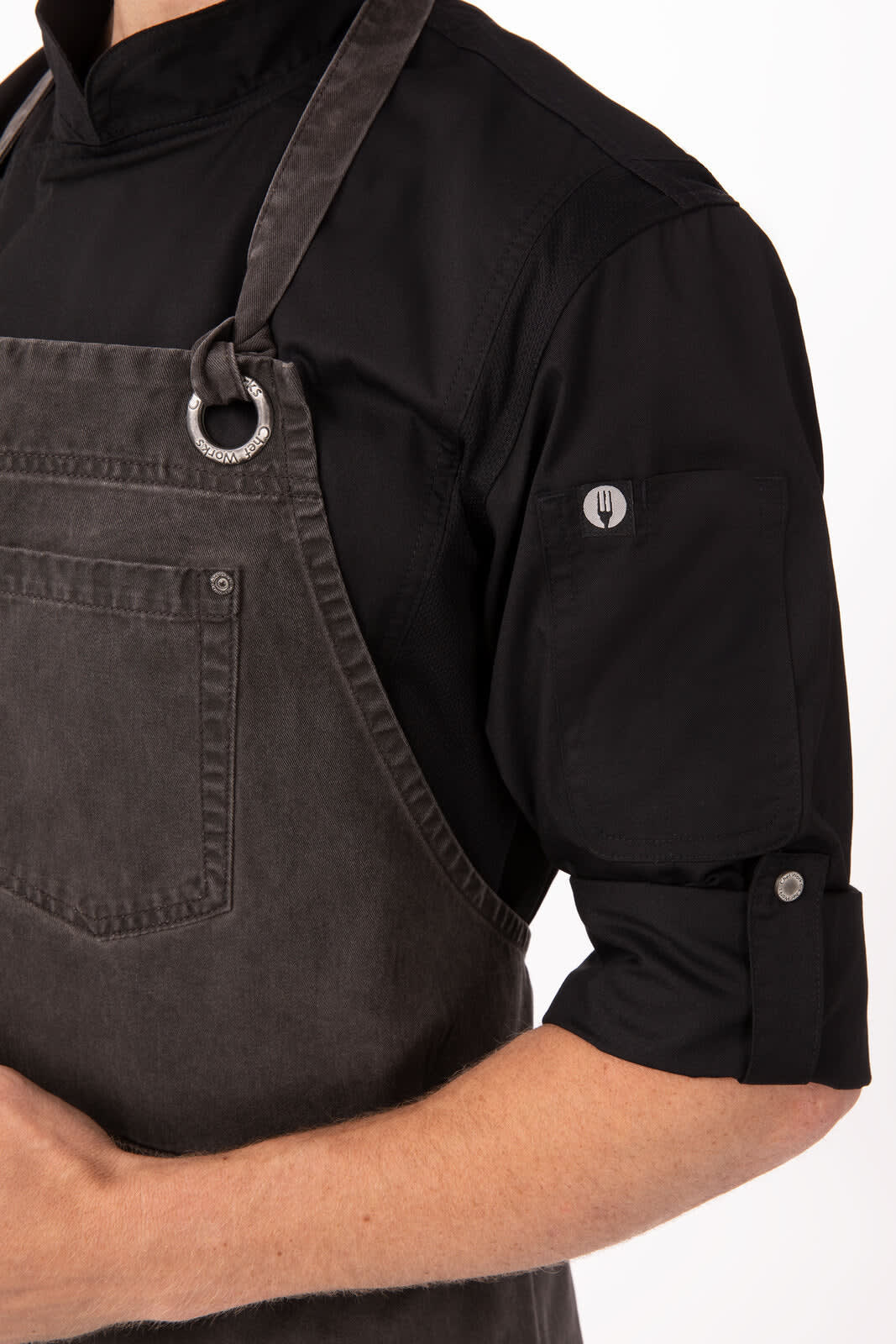 A dark grey chef's bib apron worn over a black shirt, featuring a front pocket and a circular ring detail.