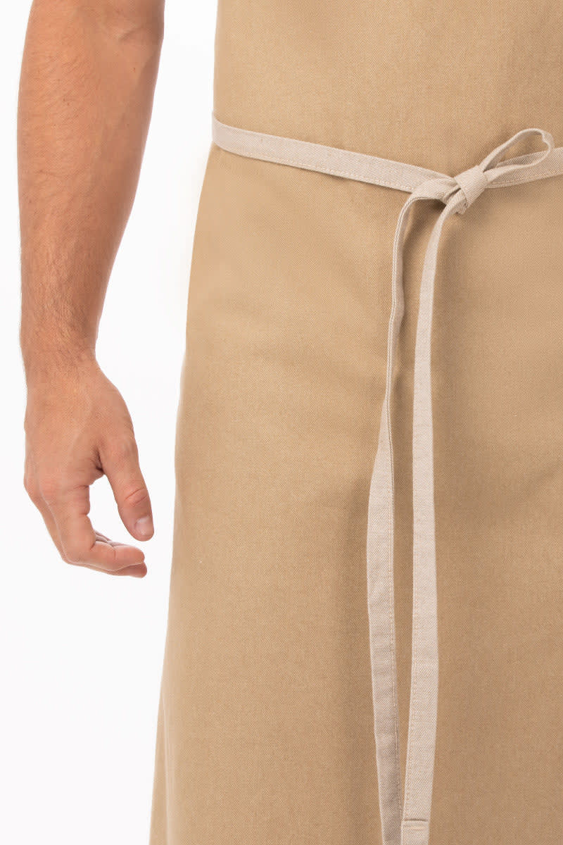 A beige bib apron with a tie waist, featuring a hand reaching towards it.
