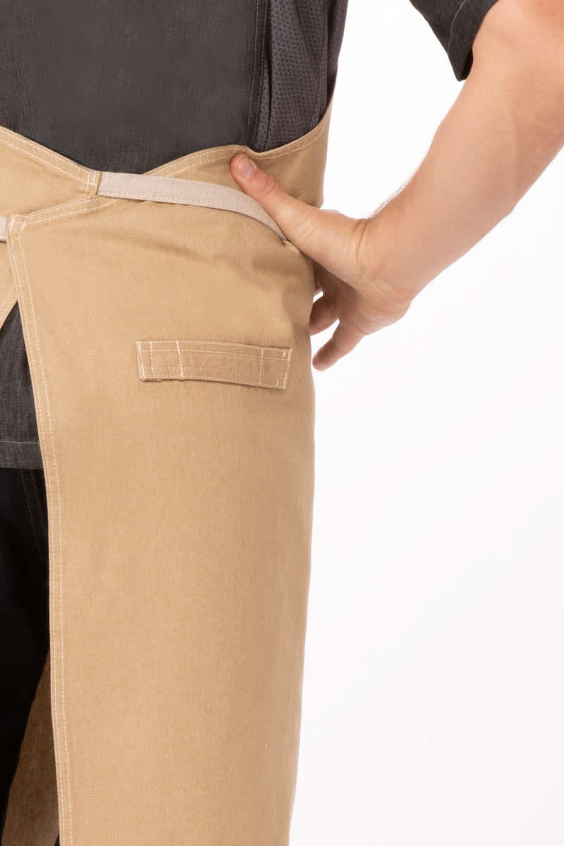 A beige chef's bib apron featuring a pocket, with a model's hand placed in the back pocket.