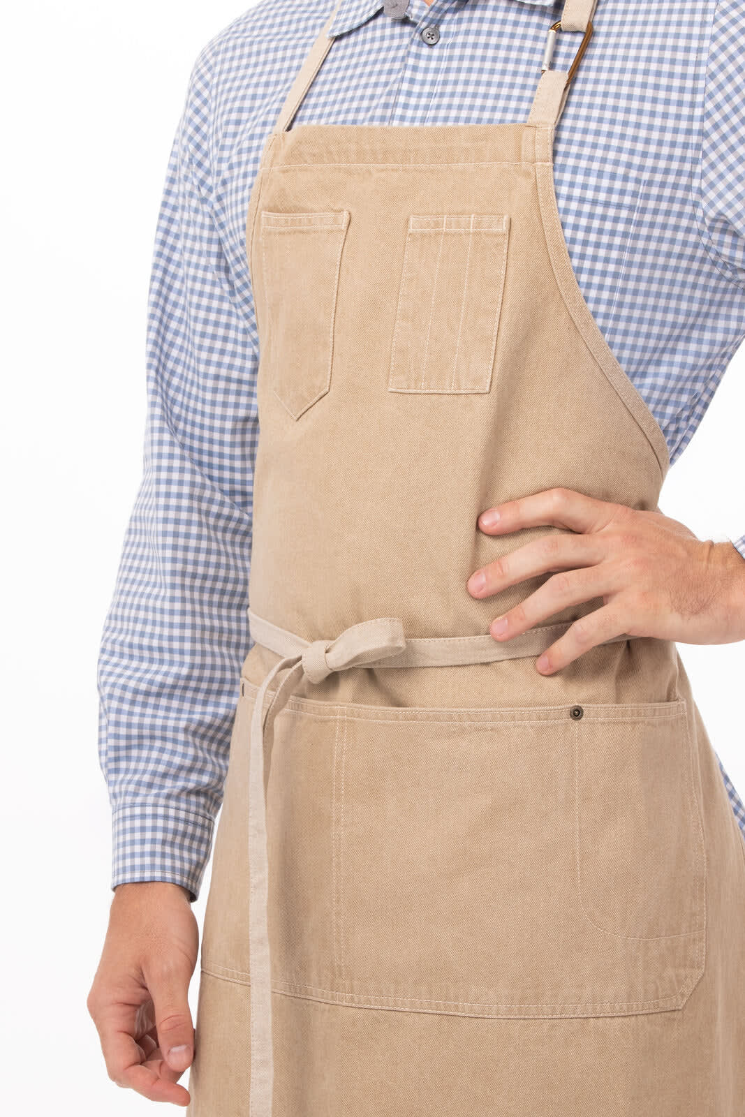 A beige bib apron with a pocket, worn over a blue and white checkered shirt. It features a tie at the waist and a logo.