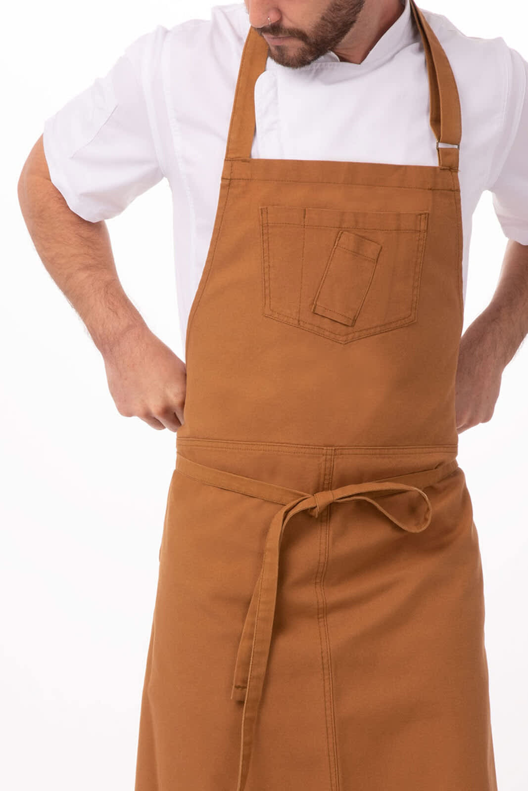 A brown bib apron features a front pocket and is worn by a person adjusting it. It has a logo branding.