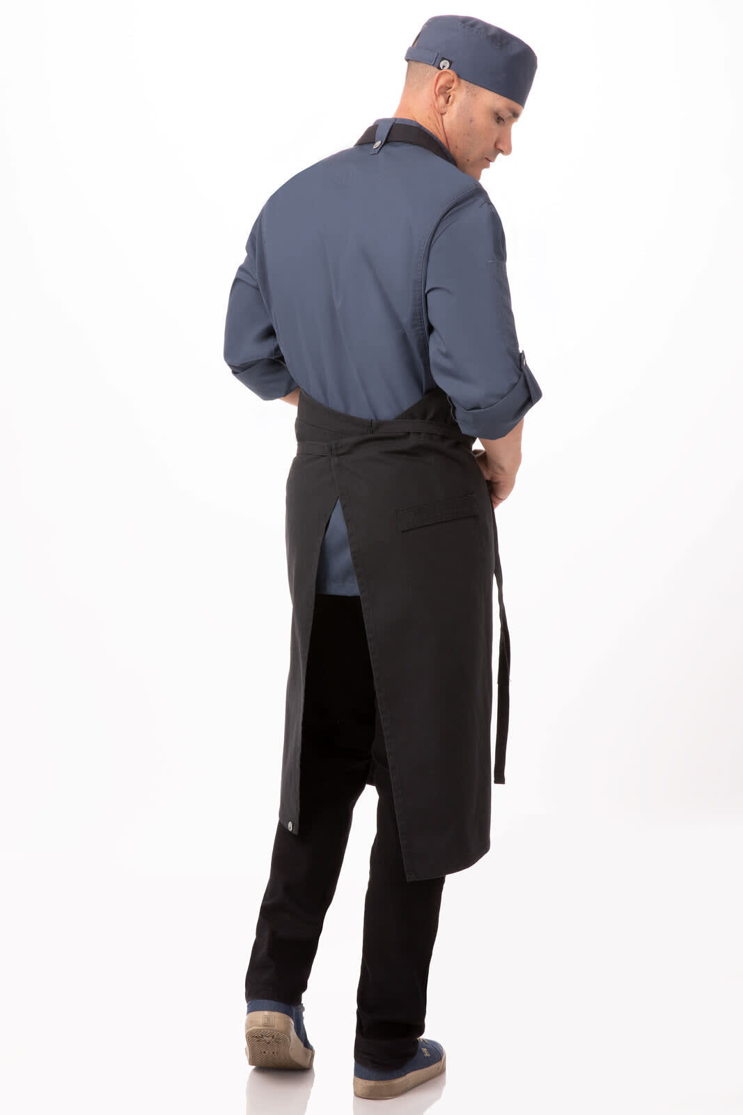 A back view of a person in a blue shirt wearing a black chef's bib apron, featuring a logo and a split design.