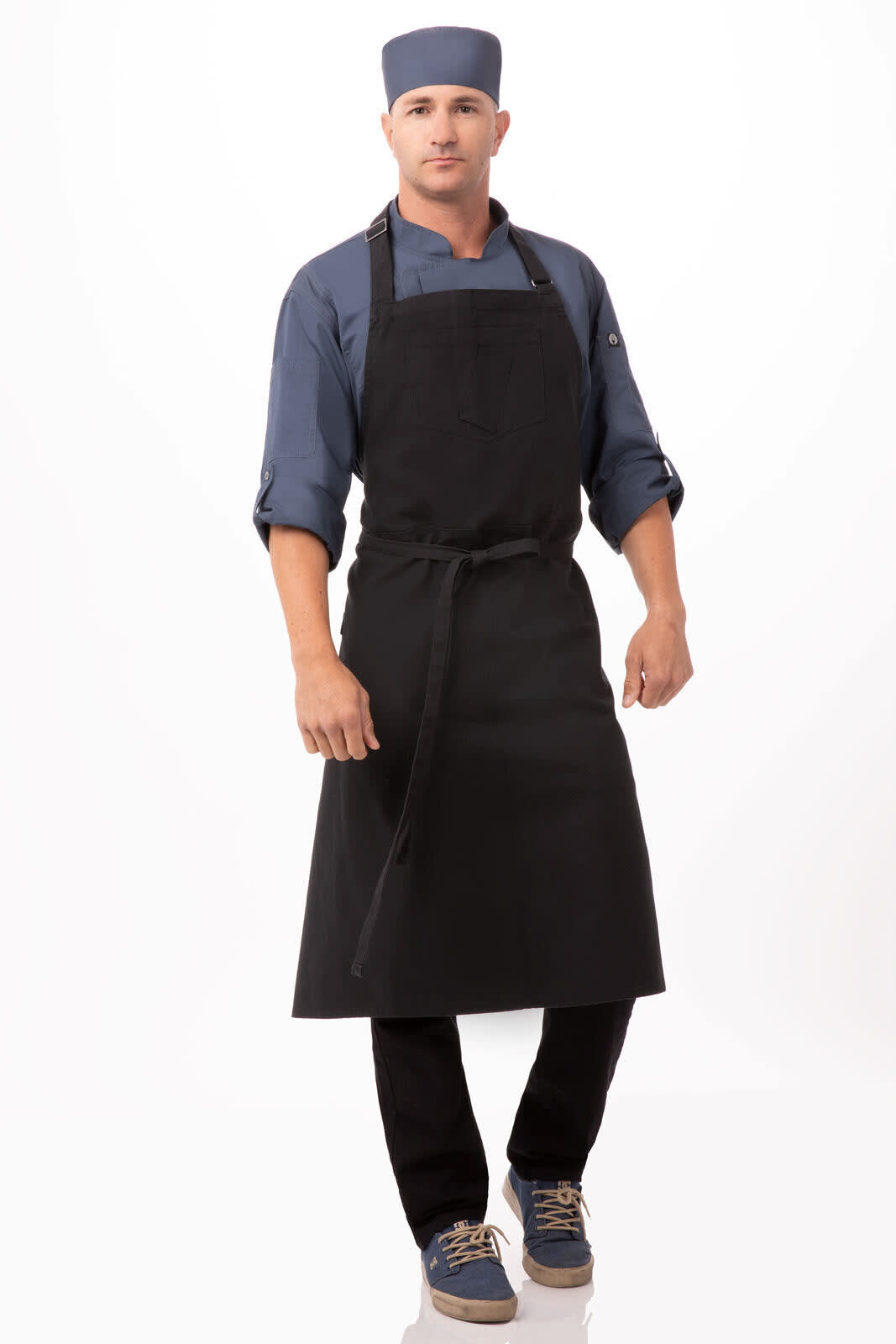 A man wearing a black bib apron and a matching cap, paired with a blue shirt and dark pants.
