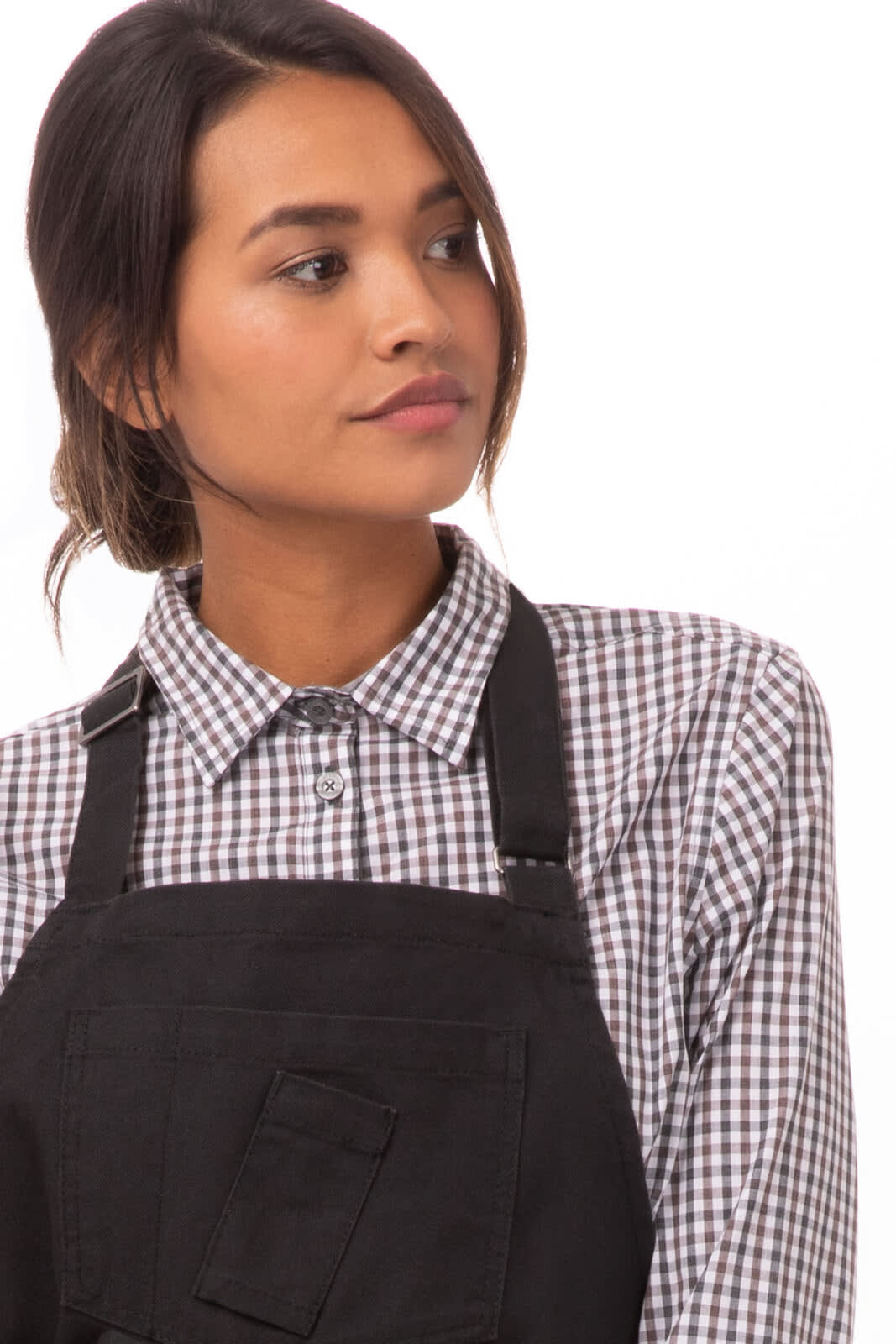 A woman wearing a black Rockford Bib Apron over a checkered shirt, featuring adjustable straps and a pocket.