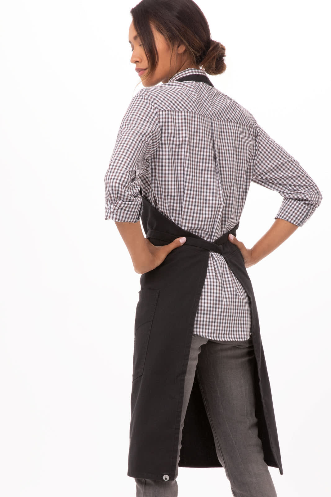 A black bib apron is worn over a checked shirt and grey pants, featuring a logo on the front.