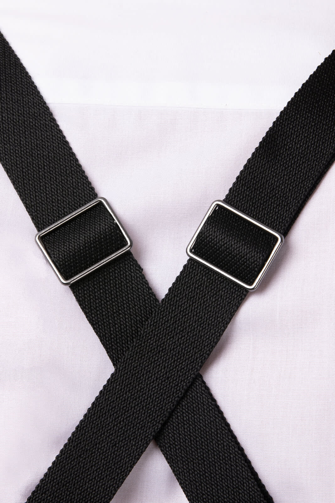 A close-up of black adjustable straps crossing over a white apron. The straps have silver hardware.