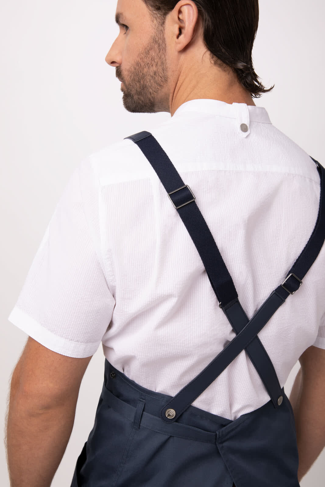 A navy blue bib apron with cross-back straps, featuring buttons, worn over a white shirt.