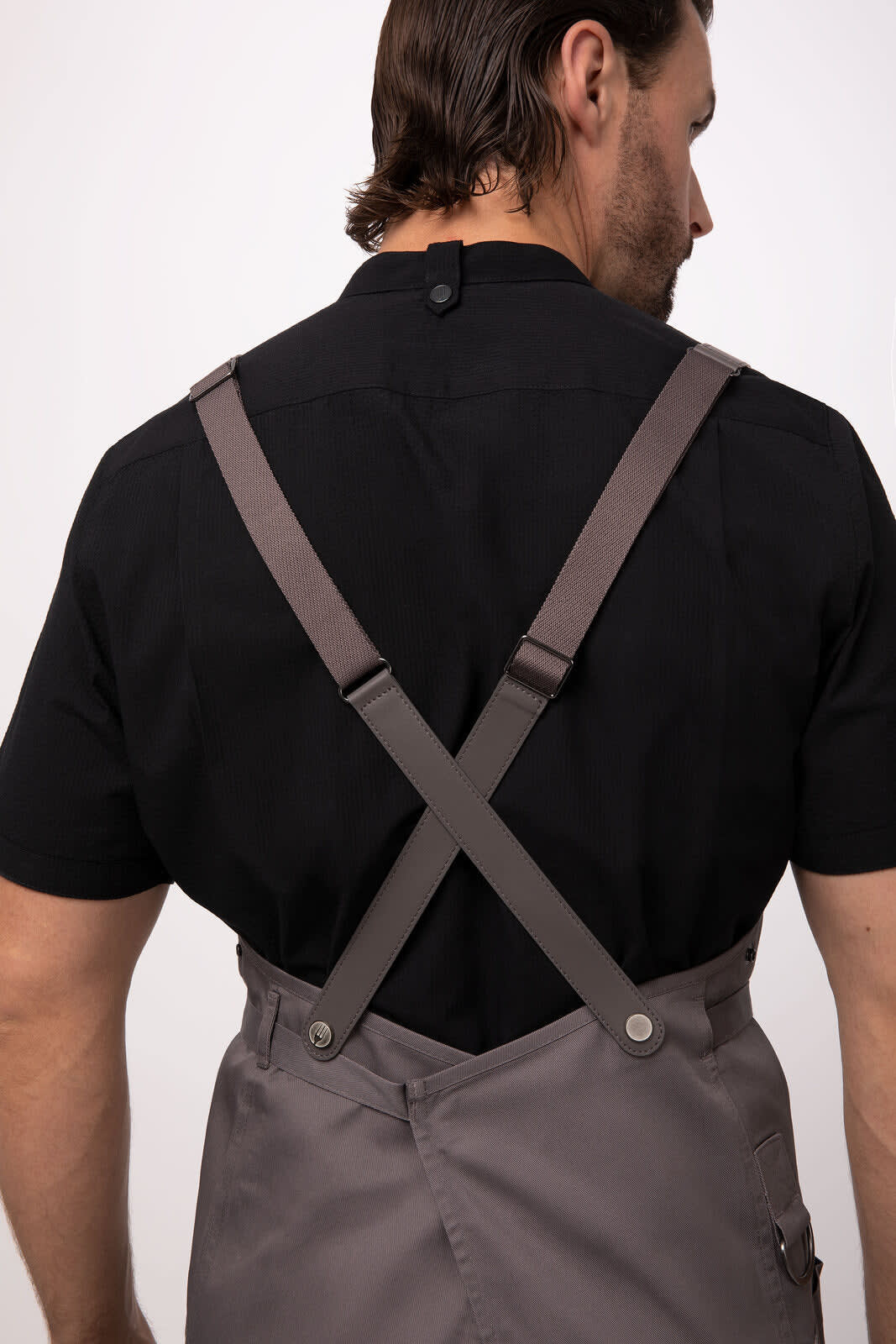 A grey bib apron with adjustable brown straps is displayed, being worn by a person from behind.