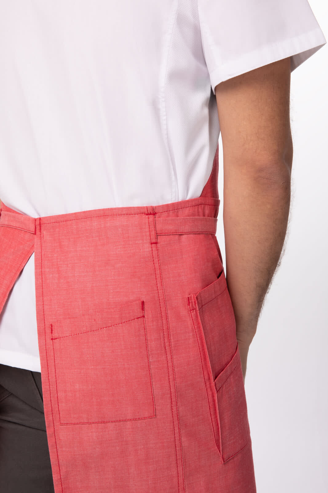 A red Medford bib apron with pockets, worn by a person in a white shirt. The design features a waistband tie.
