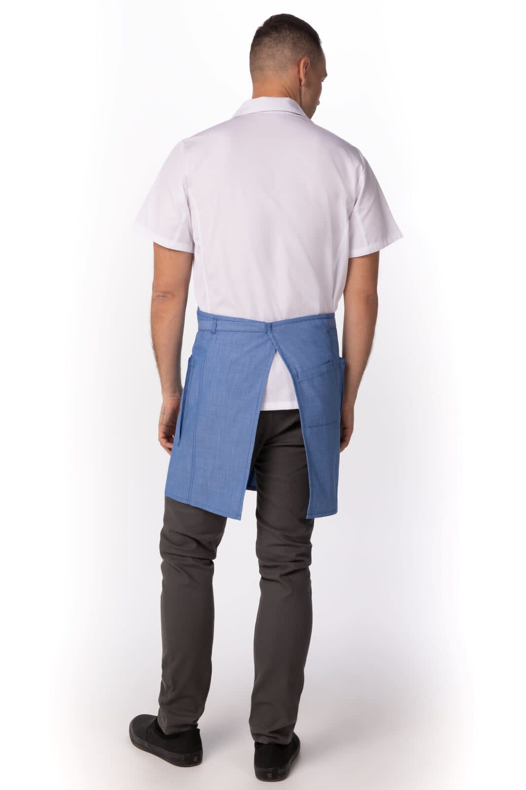 A blue bib apron seen from the back, worn over a white shirt and grey pants. It features a logo.