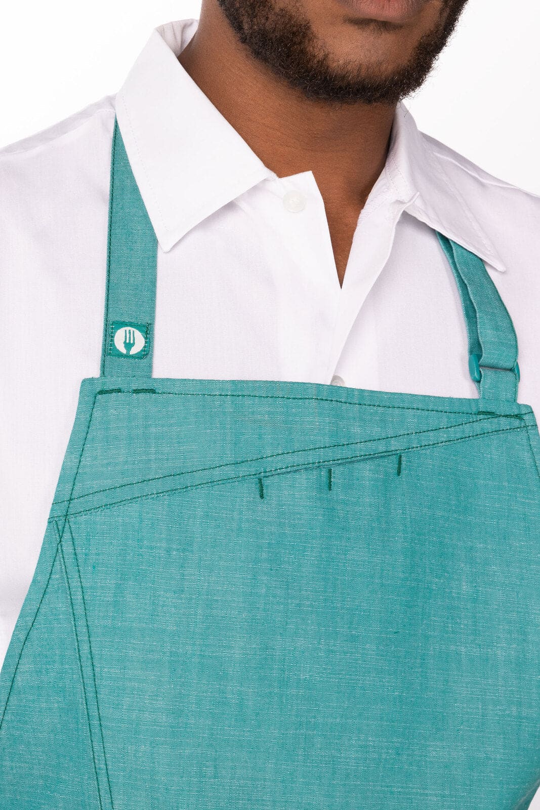 A teal bib apron with adjustable straps and a logo, worn over a white shirt.
