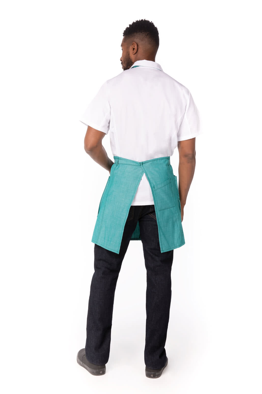 A man wearing a teal Medford Bib Apron, viewed from the back, paired with a white shirt and black pants.