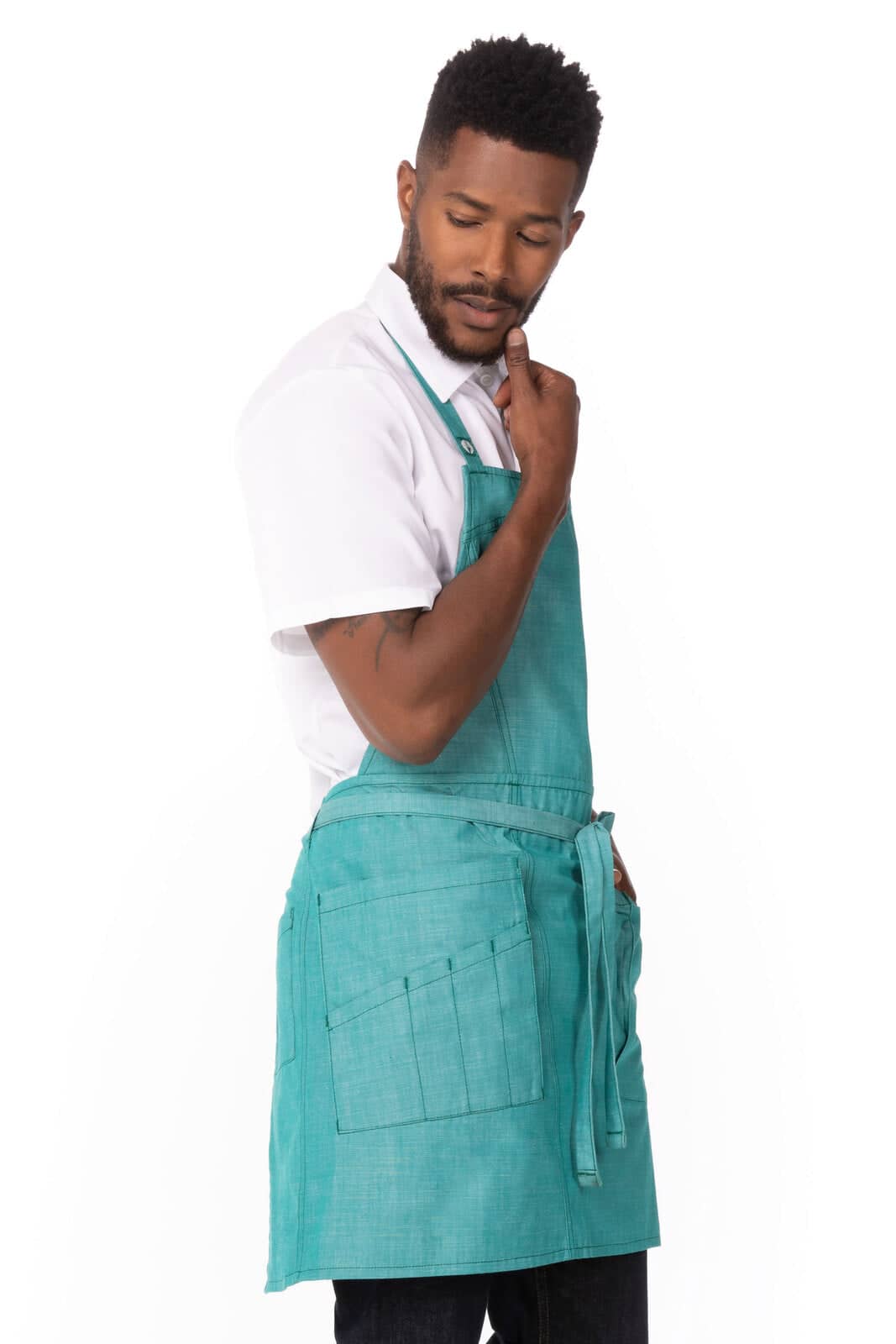 A turquoise bib apron is worn by a man, featuring pockets and a stylish design. It has a branding logo on it.