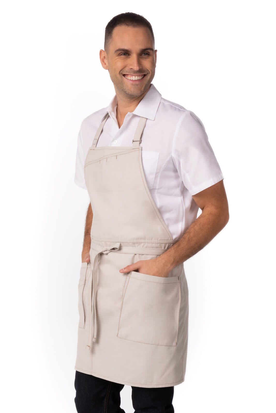 A beige bib apron with pockets, worn by a model dressed in a white shirt, showcasing a casual workwear style.