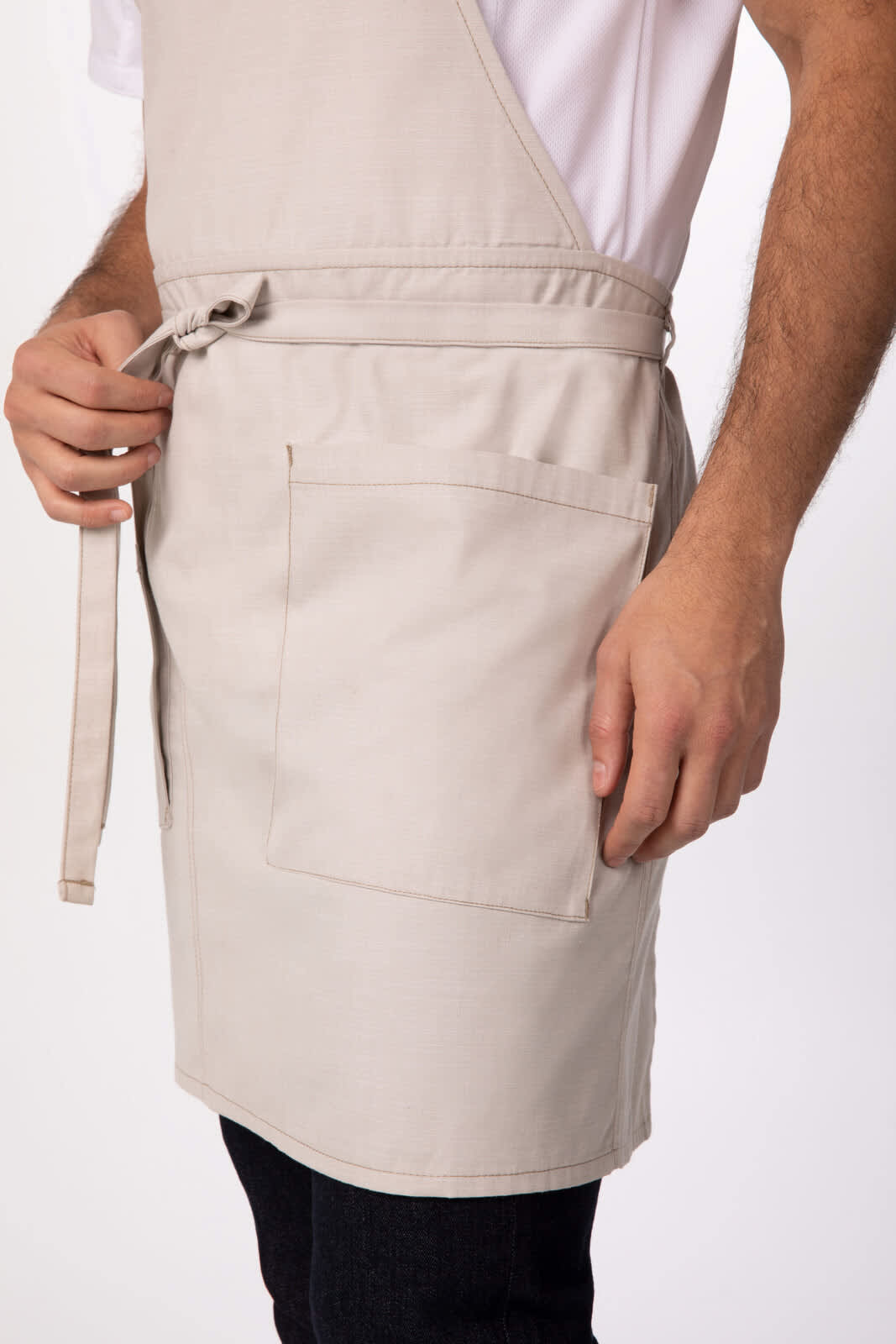 A beige Medford bib apron with a side pocket, featuring a tie waist and a model wearing it.