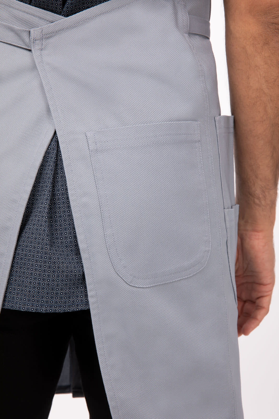 A grey bib apron featuring pockets, displayed on a person. The apron has a sleek design and a waist tie.