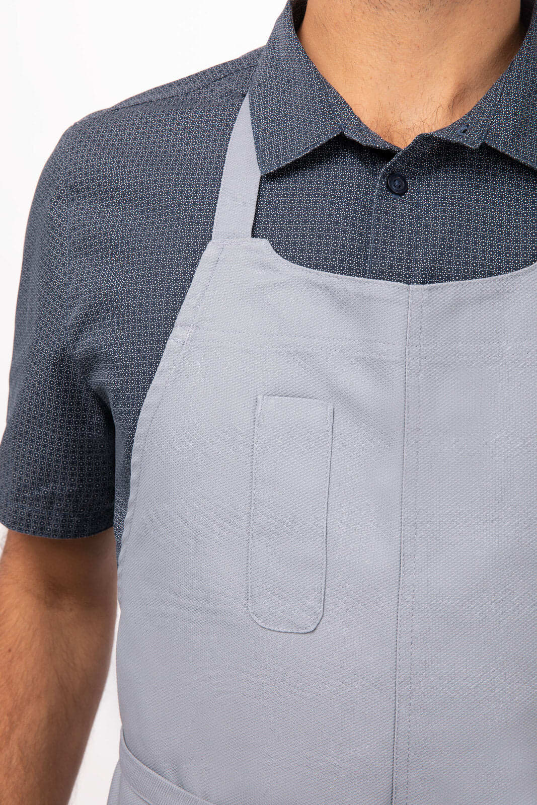 A grey Logan Bib Apron with a front pocket, worn over a patterned blue shirt.