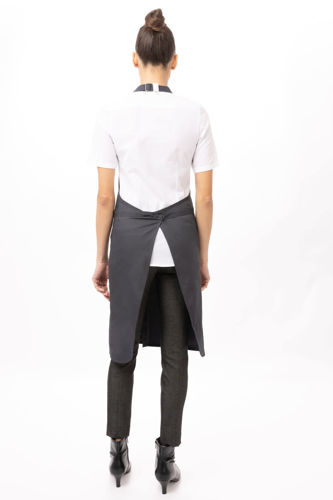 A grey Brio Bib Apron worn over a white shirt, featuring a back tie and styled with black pants and boots.