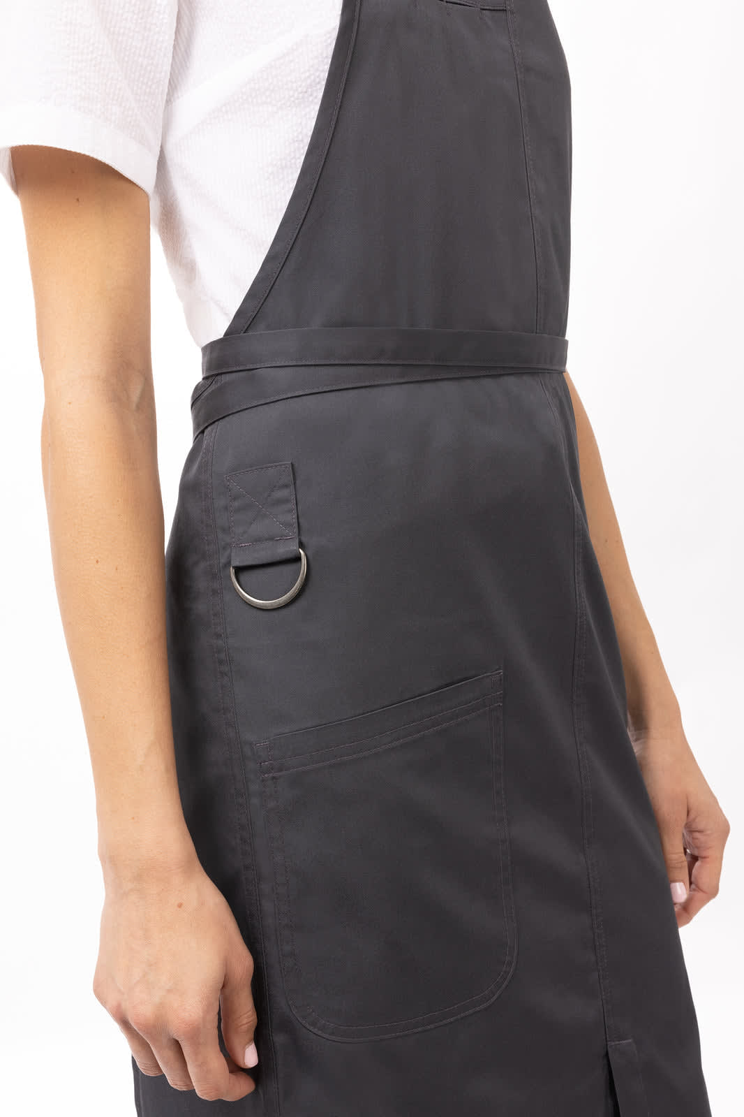A black bib apron with a pocket and a metal ring detail, worn by a person against a neutral background.