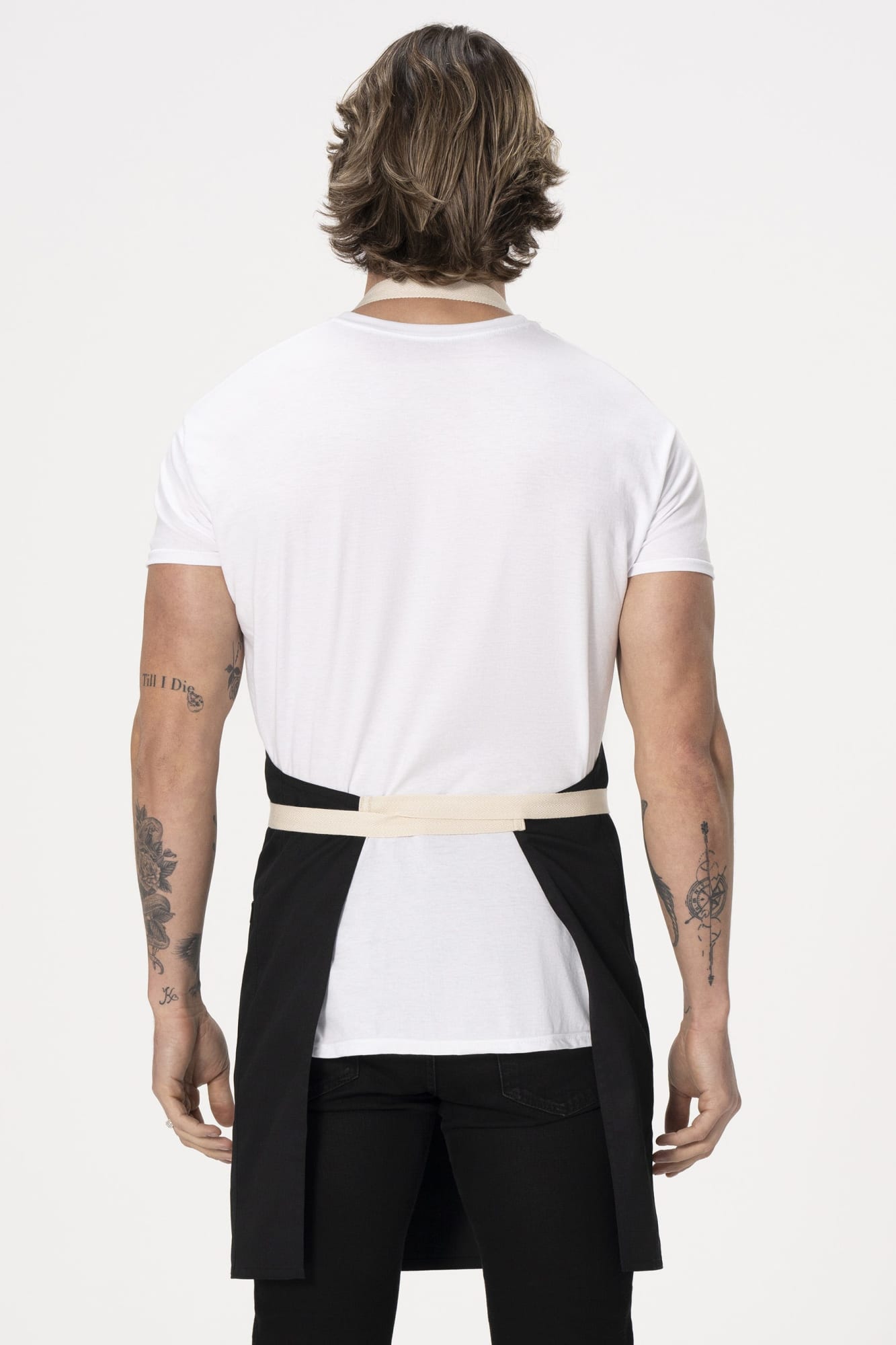 A black bib apron with a cream waist tie, displayed on a model from the back, showcasing its workwear style.