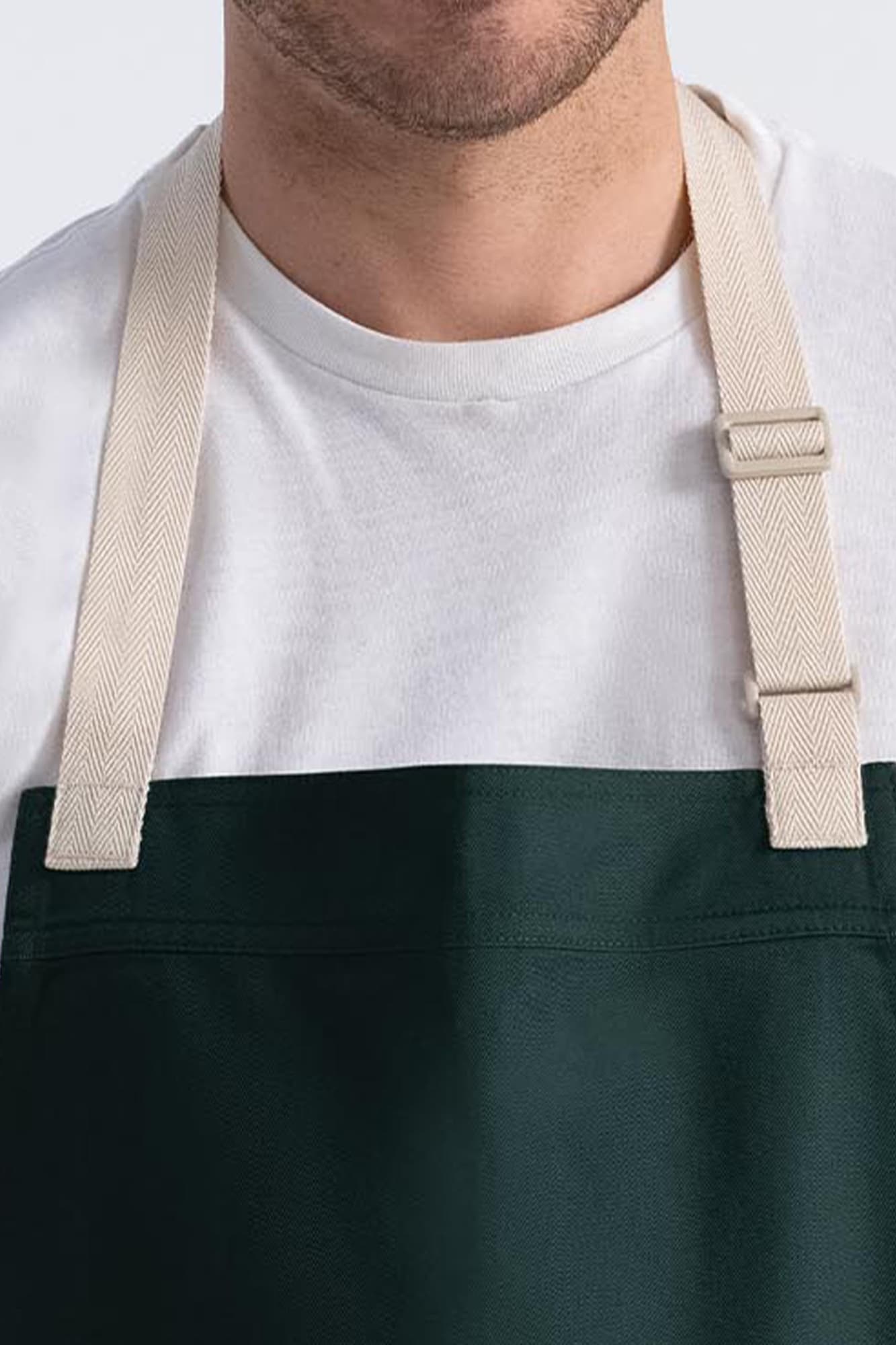 A dark green bib apron with beige straps, featuring a simple design and no visible logos.