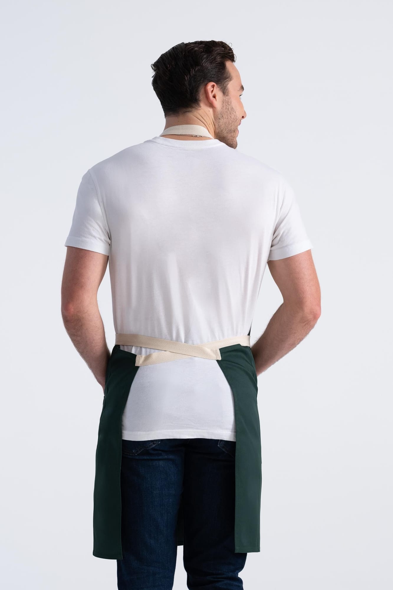 A man wearing a green Ridgewood Bib Apron, facing away, displaying its back and straps against a light background.