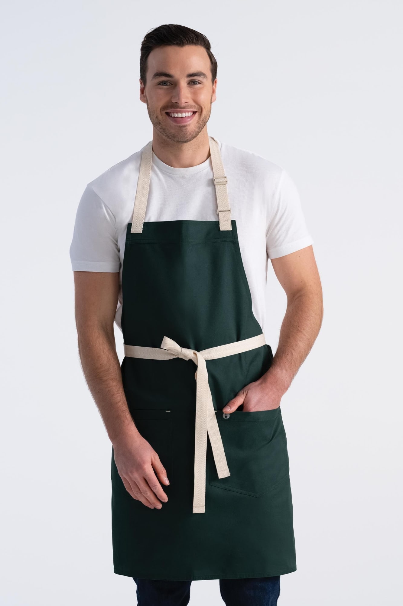 A model wearing a green Ridgewood bib apron with a beige tie and pockets, set against a plain background.
