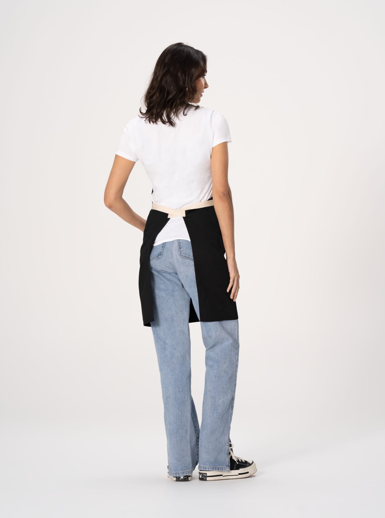 A woman wearing a black Ridgewood bib apron over a white shirt and blue jeans, showing the back of the apron.