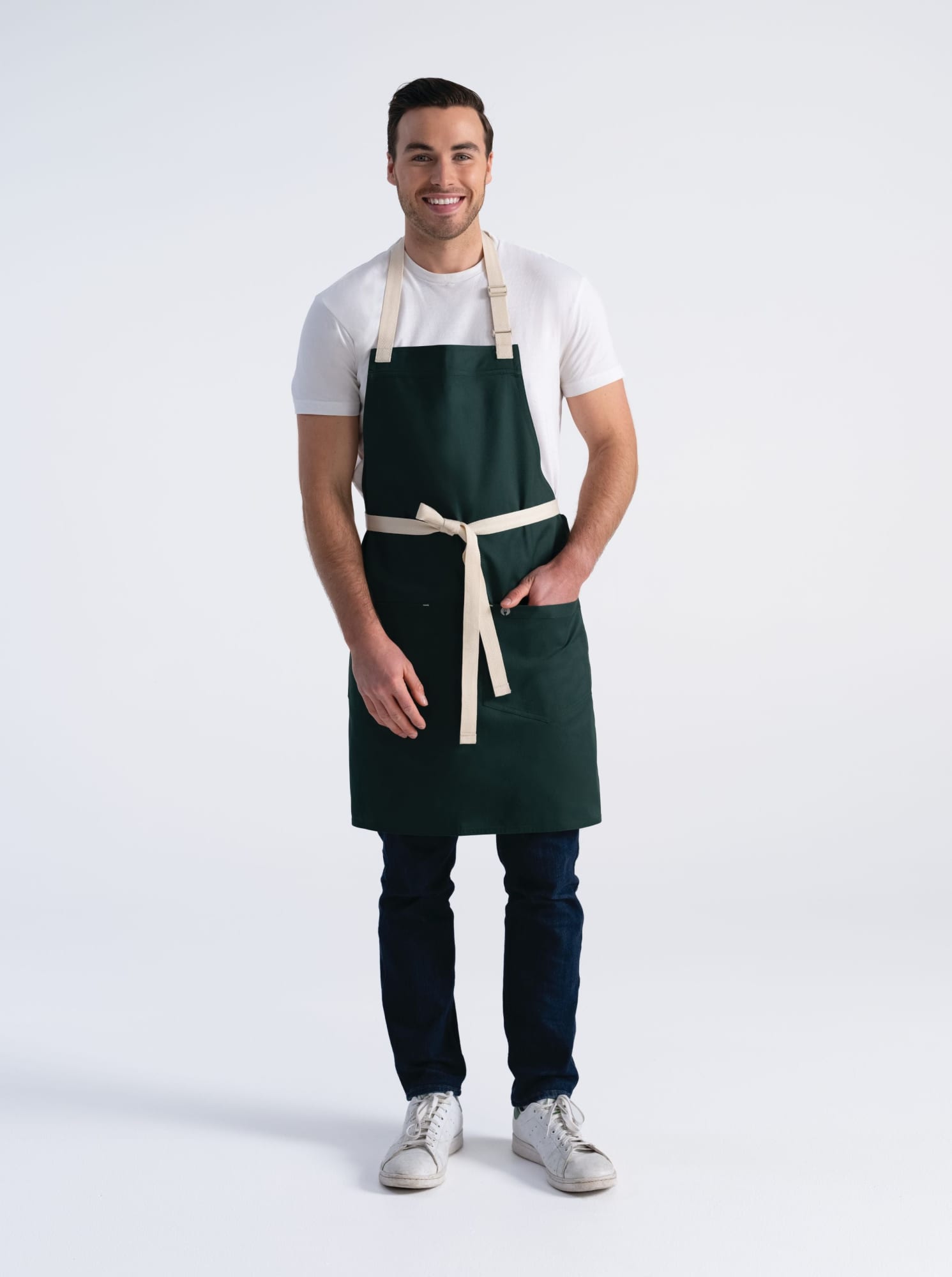 A man wearing a dark green Ridgewood bib apron with a cream waist tie, standing against a light background.