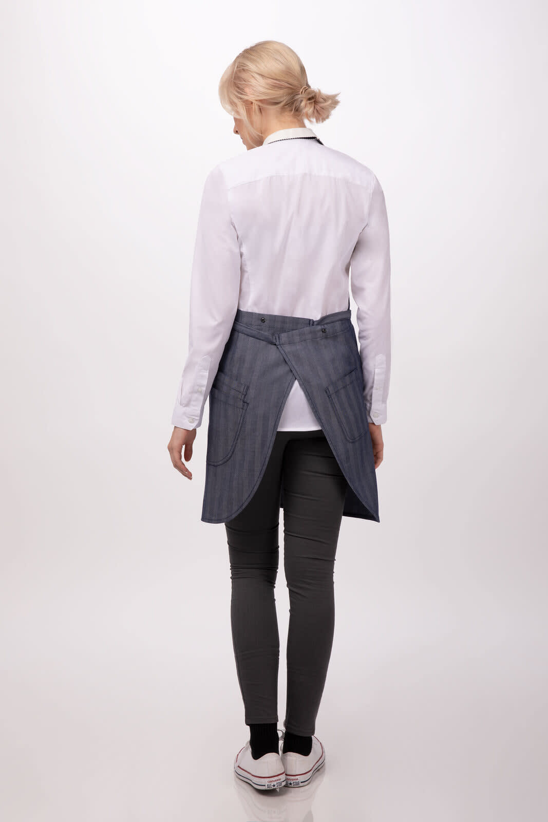 A woman is wearing a navy striped apron over a white shirt and grey pants, facing away from the camera.