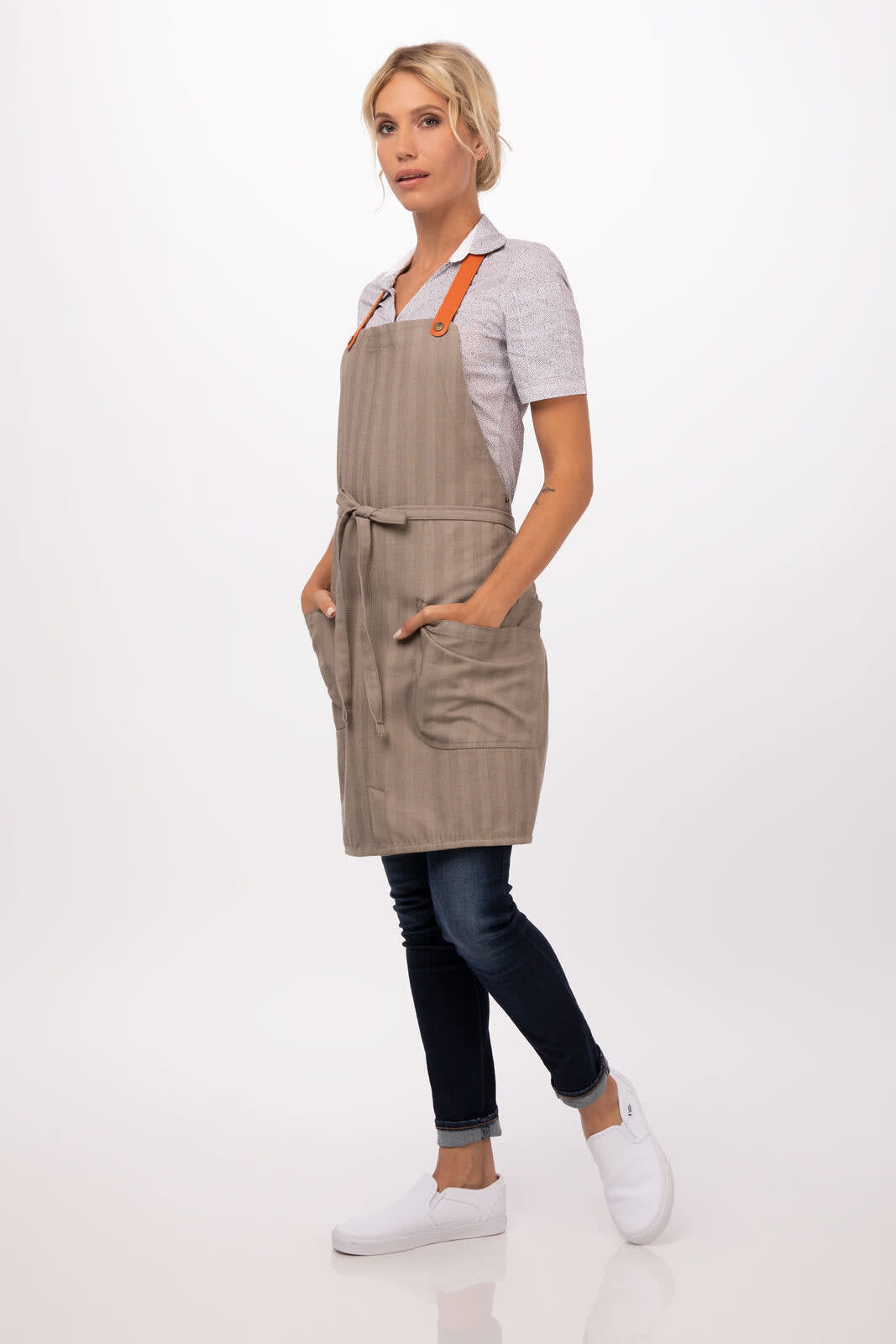 A beige and brown striped apron with orange straps, featuring pockets, worn over a casual outfit.