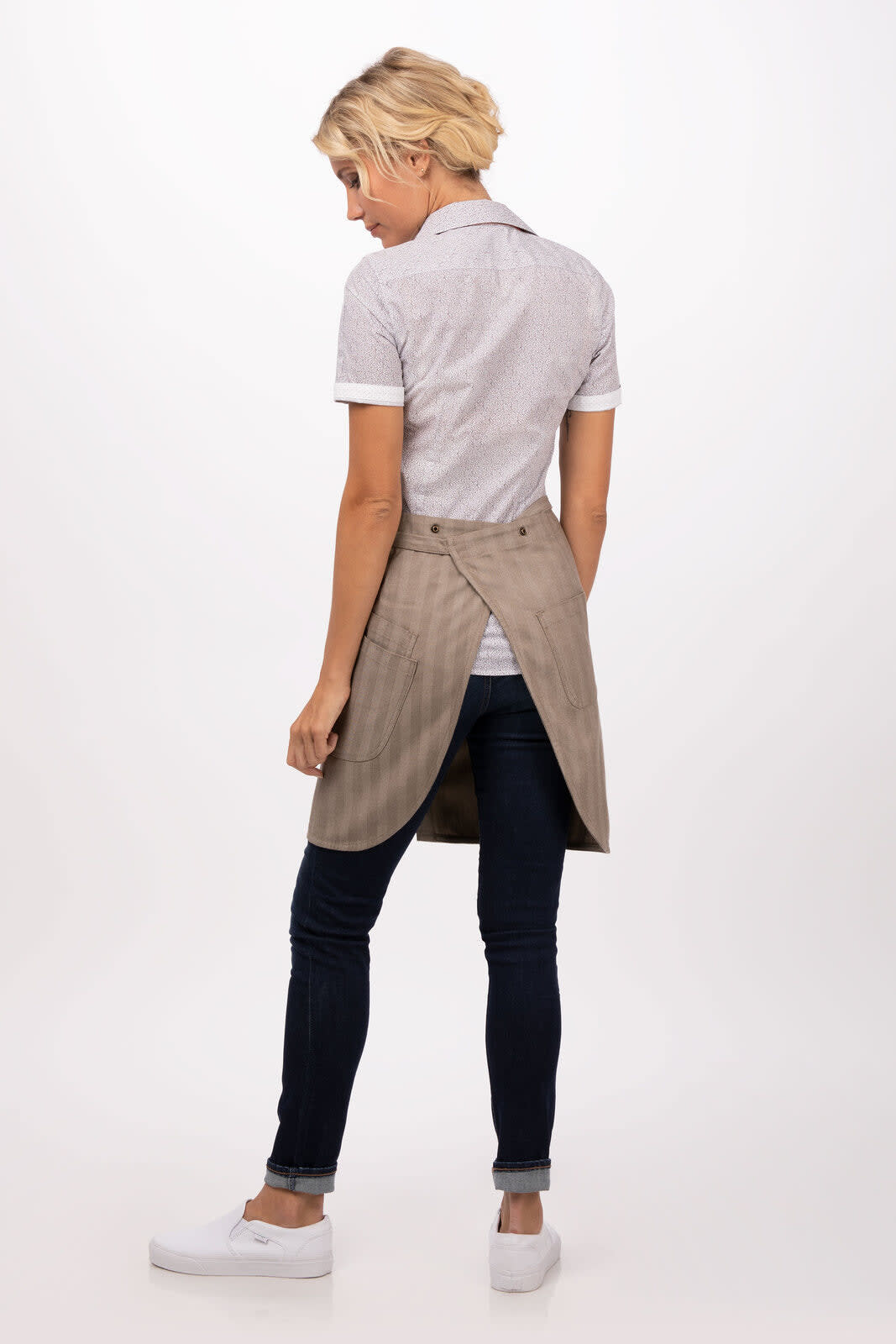 A person wearing a beige Seattle Bib Apron over a grey shirt and jeans, with a logo on the apron.